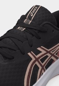 Κοντινό πλάνο ενός μαύρου αθλητικού παπουτσιού ASICS με ροζ και κόκκινο λογότυπο με σχέδιο, μαύρα κορδόνια και άσπρη σόλα σε λευκό φόντο.