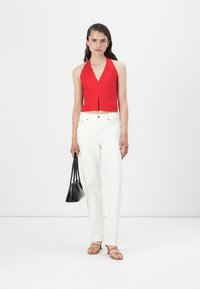 Top rouge à encolure en V profonde et fente à l'avant, associé à un jean blanc à jambes droites. Sac à bandoulière noir et sandales à brides nude.