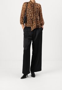 Blouse en imprimé léopard avec un col noué et des manches bouffantes, associée à un pantalon large noir et des escarpins à bout pointu. Sac à main noir inclus.