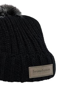 Zwarte gebreide beanie met een ribbelstructuur, voorzien van een grijze bontpompon en een beige label met de tekst "bruno banani" aan de zijkant.