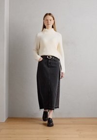 Pulover crem cu guler înalt din tricot cu nervuri, asortat cu o fustă maxi din denim negru. Fusta are o margine desfăcută și o curea cu cataramă rotundă.