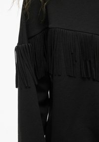 Felpa nera con dettagli in frange sulle maniche, caratterizzata da una texture morbida e una vestibilità rilassata. Design minimalista senza motivi.