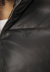 Svart skinnjakke med en jevn tekstur, med glidelås og et preget "cK"-logo på brystet.