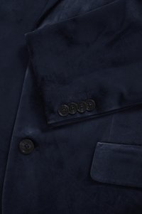 Tumesinine sametist bleiser, millel on läbiva krae, varrukal neli musta nuppu ja sileda tekstuuriga küljetasku.