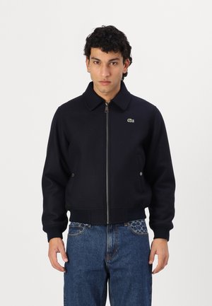Marineblauwe zip-up jack met een kraag, geribde manchetten en boord. Heeft een klein groen Lacoste-logo op de linkerkant van de borst.
