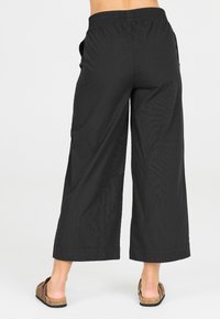 Svarta, vida byxor med resårmidja och sidofickor. Tillverkade av lättviktsmaterial, med en slät yta och sydd nederkant.