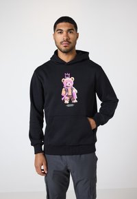 Schwarzer Hoodie aus weichem Material mit einem bunten Bären-Graphic, der eine Krone und eine Sprühdose hält, vorderer Kängurutasche, gerippten Bündchen.