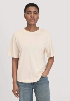 T-shirt in cotone beige con collo rotondo e maniche corte, caratterizzato da una vestibilità comoda e una texture liscia. Indossato con jeans in denim blu.