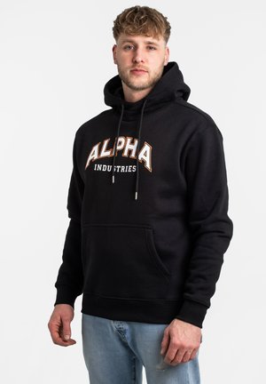 Sudadera con capucha negra con "ALPHA INDUSTRIES" impreso en naranja y blanco. Presenta cordones, un bolsillo frontal y una textura de tela suave.