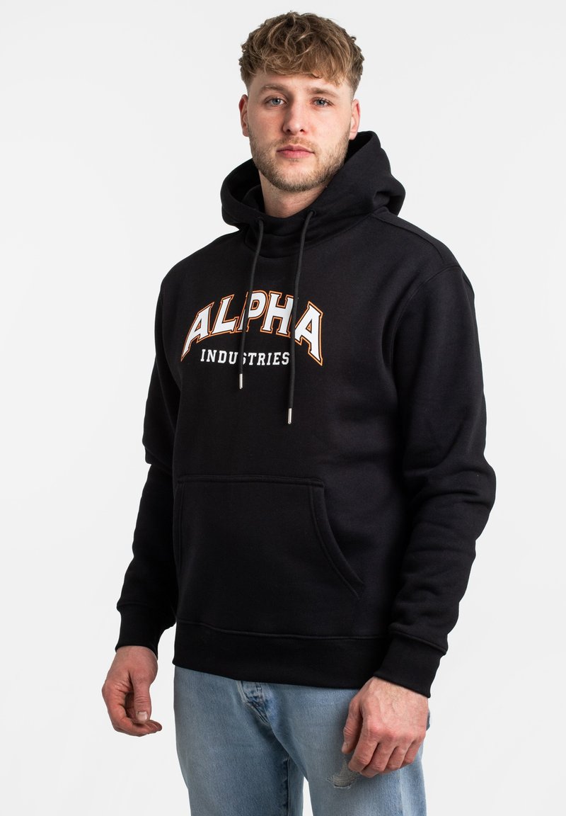 Felpa nera con cappuccio con la scritta "ALPHA INDUSTRIES" stampata in arancione e bianco. Presenta cordini, una tasca frontale e una texture di tessuto morbido.