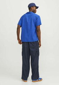 Chemise courte à manches courtes bleu, pantalon cargo marine, baskets bleues et casquette marine. Présente une coupe décontractée et de nombreuses poches sur le pantalon.