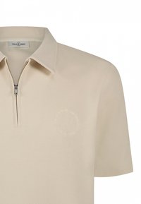 Beige polo shirt met korte mouwen, ritssluiting bij de kraag en een cirkelvormig logo op de borst. Soepele textuur en een eenvoudig, modern ontwerp.