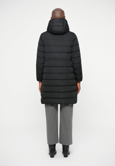 Black puffer coat with a hood, featuring vertical quilted panels and a straight cut, paired with gray wide-leg trousers and black ankle boots.