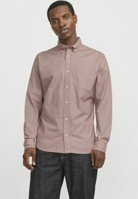 Camisa de manga larga en un suave color malva, con cuello abotonado, bolsillo delantero y botones blancos, combinada con pantalones de mezclilla oscuros. Textura suave.