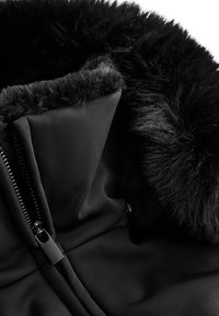 Crna vanjska odjeća s mekim crnim krznom oko vrata, glatka tkanina s mat završnom obradom i zatvaračem sprijeda.