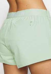 Pantalones cortos deportivos de color verde claro con una cintura reforzada, con el logo de "Calvin Klein" y un bolsillo con cremallera en la parte posterior. Textura suave.