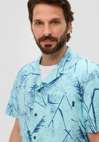 Camisa de manga corta y cuello en tela de color azul claro, con un estampado abstracto en azul contrastante, botones y un detalle de bolsillo en la parte frontal.