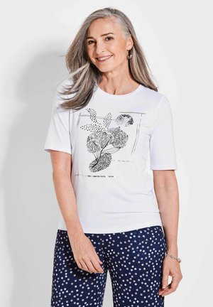 Witte t-shirt met korte mouwen met een zwart bloemen grafisch ontwerp. Gepaarde met marineblauwe broek versierd met witte stippen.