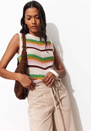 Femme portant un haut sans manches en maille rayé et un pantalon beige, ajustant sa taille, avec un sac à bandoulière marron à motif léopard.