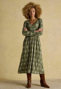 Zelené maxi šaty s dlhými rukávmi, výstrihom do V a zhromaždeným pásom, skombinované s hnedými koženými cowboy čižmami na opätku.