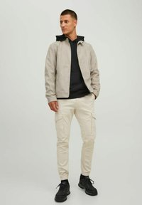 Light grey suede jacket with black hooded sweatshirt, cream cargo pants, and black sneakers. Casual outfit with multiple pockets and textured fabric.