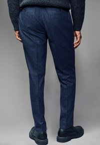 Sötétkék, szabott nadrág texturált anyagból, slim fit szabás, keskenyedő lábak, kettős hátsó zsebekkel, fekete cipővel párosítva.