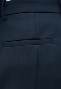 Κοντινό πλάνο τσέπης από σκούρο μπλε, ραμμένο παντελόνι με θηλιά για ζώνη και κεντρική ραφή.