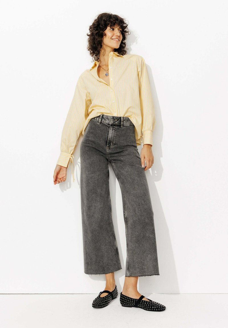 Chemise jaune à rayures avec des manches amples, jean large gris taille haute et ballerines noires à pois avec design découpé.