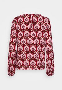 Blusa de manga larga en tejido rojo con un estampado floral en rosa y verde, con un corte en forma de ojo de cerradura en la parte posterior y mangas fruncidas.