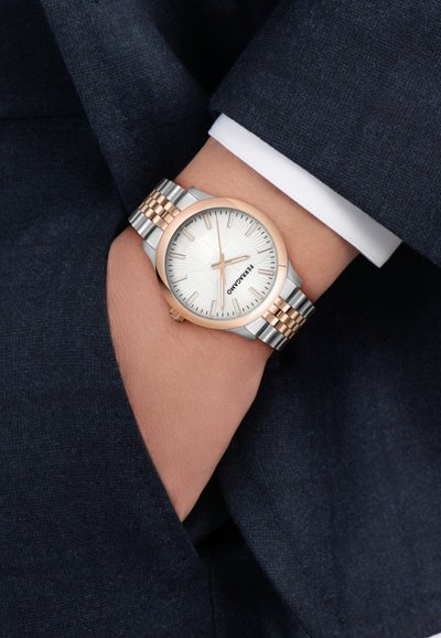 Srebrny i różowozłoty zegarek na nadgarstek z okrągłą srebrną tarczą, teksturowanym środkiem i indeksami cyfrowymi. Bransoleta z metalowych ogniw z naprzemiennymi kolorami.