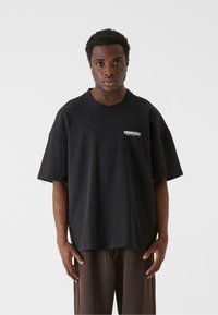 Sort oversized t-shirt lavet af bomuld. Har korte ærmer, rund hals og hvidt logo print på venstre bryst. Afslappet design.