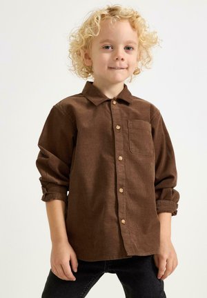 Camicia in velluto a coste marrone con colletto button-down, tasca frontale e maniche arrotolate. Presenta bottoni in legno e una superficie texture.