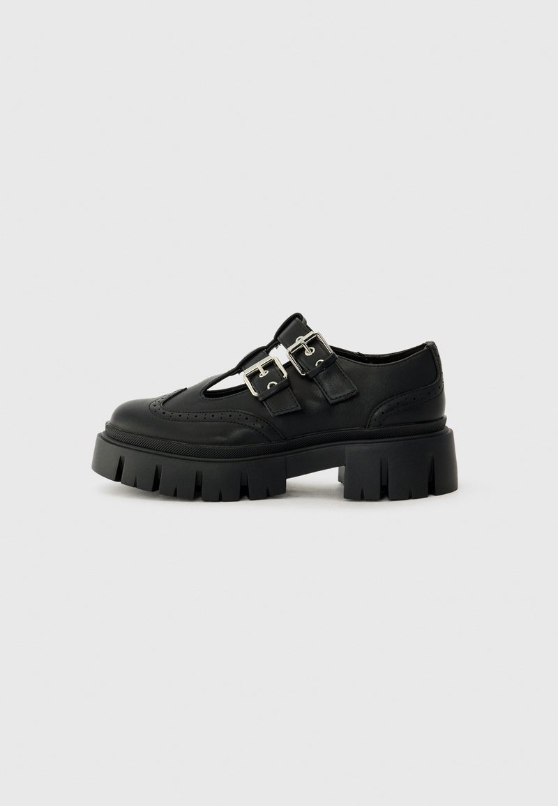 Chaussure en cuir noir avec design découpé, accents de double boucle en argent et semelle plateau épaisse avec bords crantés.