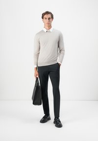 Vaaleanharmaa neule, joka on kerroksittain valkoisen kauluspaidan päällä, yhdistetty mustiin slim-fit-housuihin ja mustiin kenkiin, pitäen mustaa laukkua.