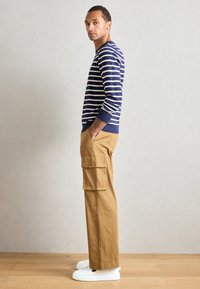 Navy and white striped sweater, crew neck; tan cargo pants with side pockets; white sneakers. Model poses sideways against a plain background.