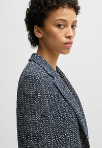 Navy and white textured blazer with a notched lapel and open front. Made from a blend of materials, featuring a structured fit.
