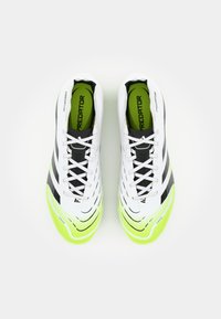 Crampons de football blancs avec des rayures noires et des accents vert fluo. Matériau supérieur lisse, capuchon de orteil texturé et système de laçage standard.