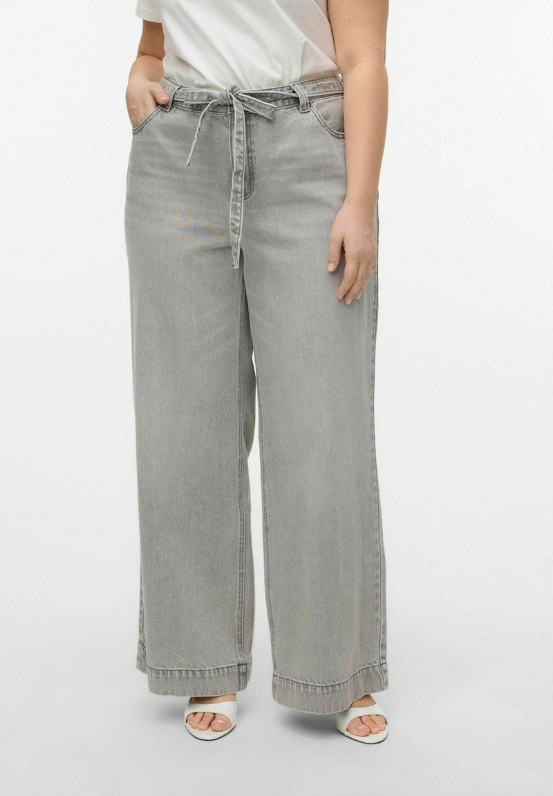 Pantalones de mezclilla gris de pierna ancha con cintura elástica y un ajuste relajado. Textura suave, dobladillo sin terminar, combinados con sandalias blancas de tacón.