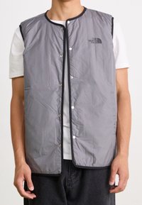 Šedá izolační vesta s kulatým výstřihem, zapínáním na patentky a černými detaily. Na levé straně se nachází logo "The North Face".