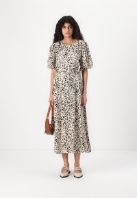 Løveprint midi-kjole med puffede ærmer, indsnævret talje og en flydende skørt. Stylet med en brun skuldertaske og beige sko.