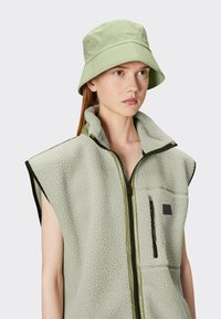 Gilet en polaire vert clair avec un devant zippé, un grand col et une poche poitrine ; associé à un chapeau seau vert clair assorti.