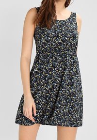 Kukallinen kesämekko, jossa on vartalonmyötäinen yläosa, liehuva helma, tumma tausta monivärisillä kukilla ja pehmeä kangaspinta.