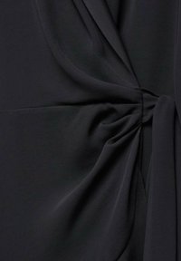 Tissu noir avec un détail de nœud froncé créant des plis et des drapés doux, montrant la texture et les lignes de couture.