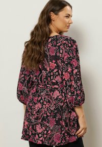 Blusa nera con motivi floreali e paisley rosa. Presenta maniche lunghe a sbuffo e vita annodata, realizzata in tessuto leggero.