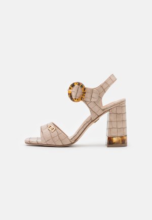 Sandale en cuir beige embossé crocodile avec un accent en écaille de tortue arrondi, une bride à la cheville et un talon bloc transparent.