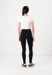 Zwarte leggings met een hoge taille, gecombineerd met een witte top met korte mouwen. Het model draagt zwart-witte sneakers. Glad, aansluitend materiaal.