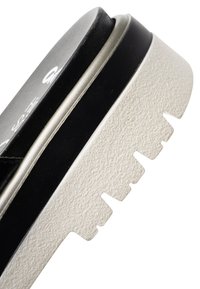 Primer plano de la suela de un zapato en blanco y negro con surcos profundos y una parte inferior blanca texturizada para mayor tracción.