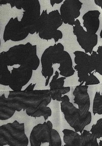 Motif floral noir sur un tissu beige clair, présentant une texture en maille avec des formes irrégulières et des bords doux tout au long.