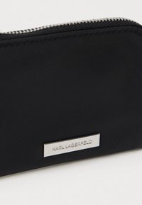 Ingrandimento di un sacchetto nero con una zip argentata e una piccola placca metallica incisa con la scritta "KARL LAGERFELD."