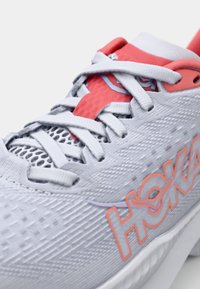 Baskets de course gris clair avec des lacets blancs et des détails en maille. Équipées d'un logo rose et orange et d'une surface texturée pour une meilleure adhérence.